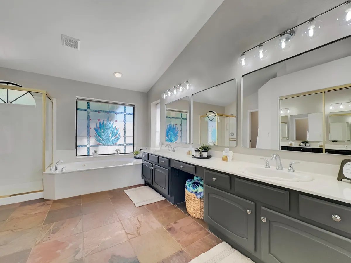 A spacious spa-like bathroom featuring large mirrors, a stained glass window that bathes the room in gentle light, a double vanity, and a soaking bathtub. The airy ambiance hints at a peaceful self-care experience.
