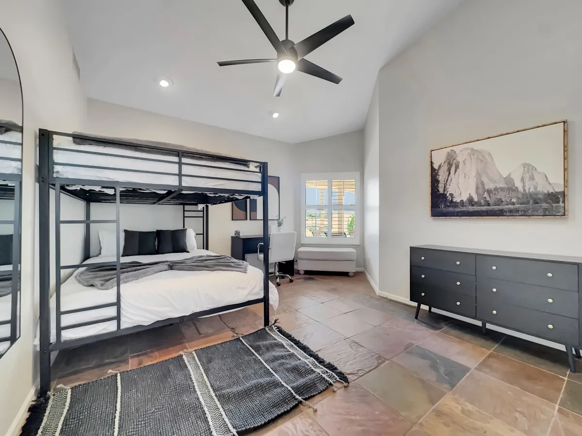 A cozy bunk bedroom with a dedicated desk area, modern artwork on the wall, and a dresser. The room feels functional yet inviting, suitable for families or individuals needing both rest and workspace.
