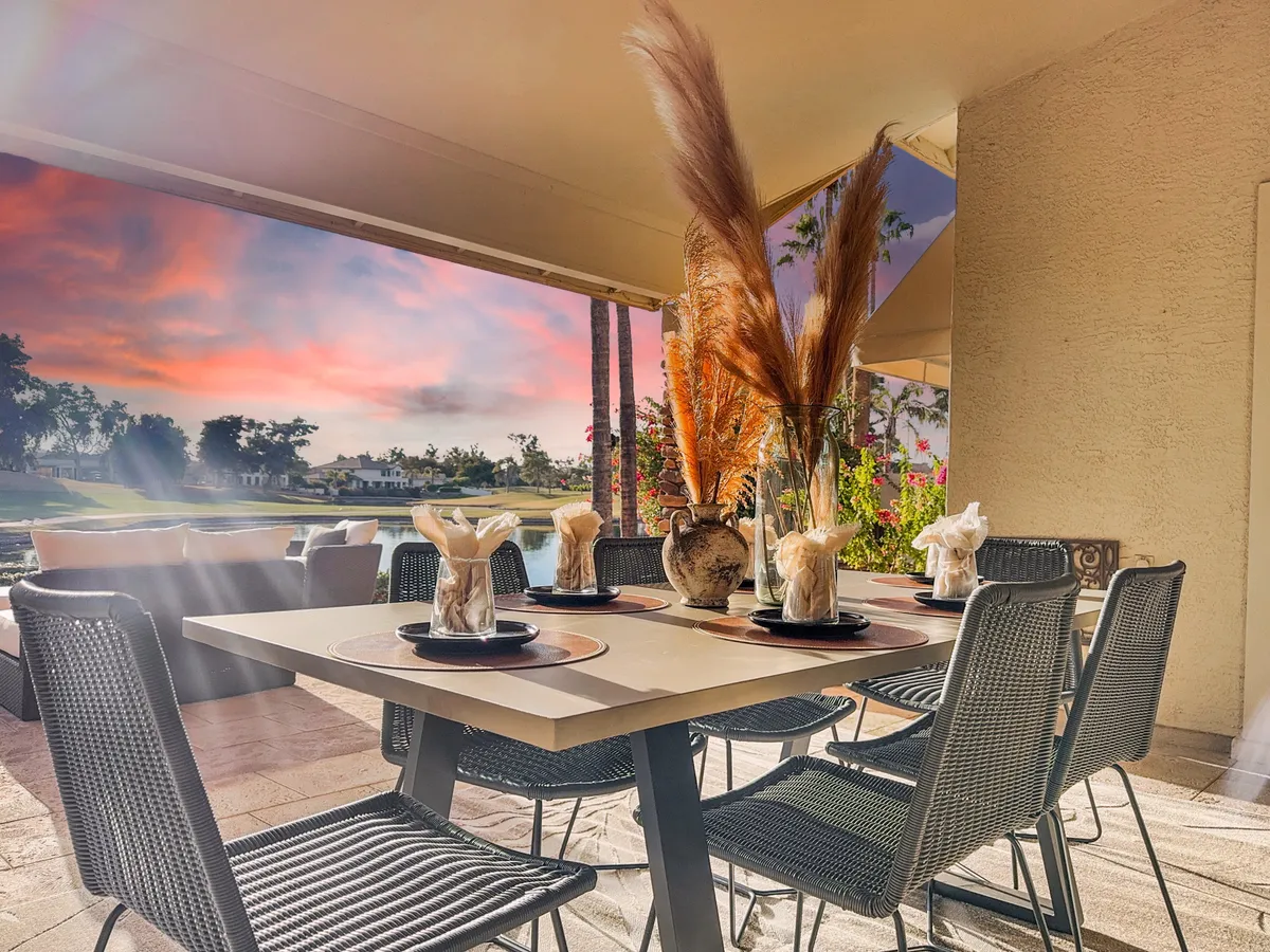 An elegant outdoor dining table adorned with a decorative vase and pampas grass, set against a stunning sunset sky. The setting evokes alfresco dining experiences and relaxed evenings with friends or family.