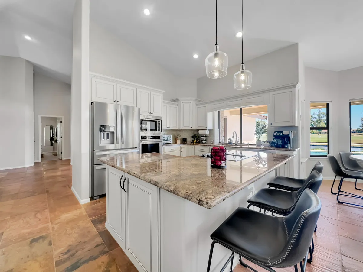 A contemporary kitchen scene with granite countertops, sleek appliances, and bar stools set up by the breakfast bar. Large windows flood the area with natural light, creating an inviting ambiance for casual dining and coffee chats.