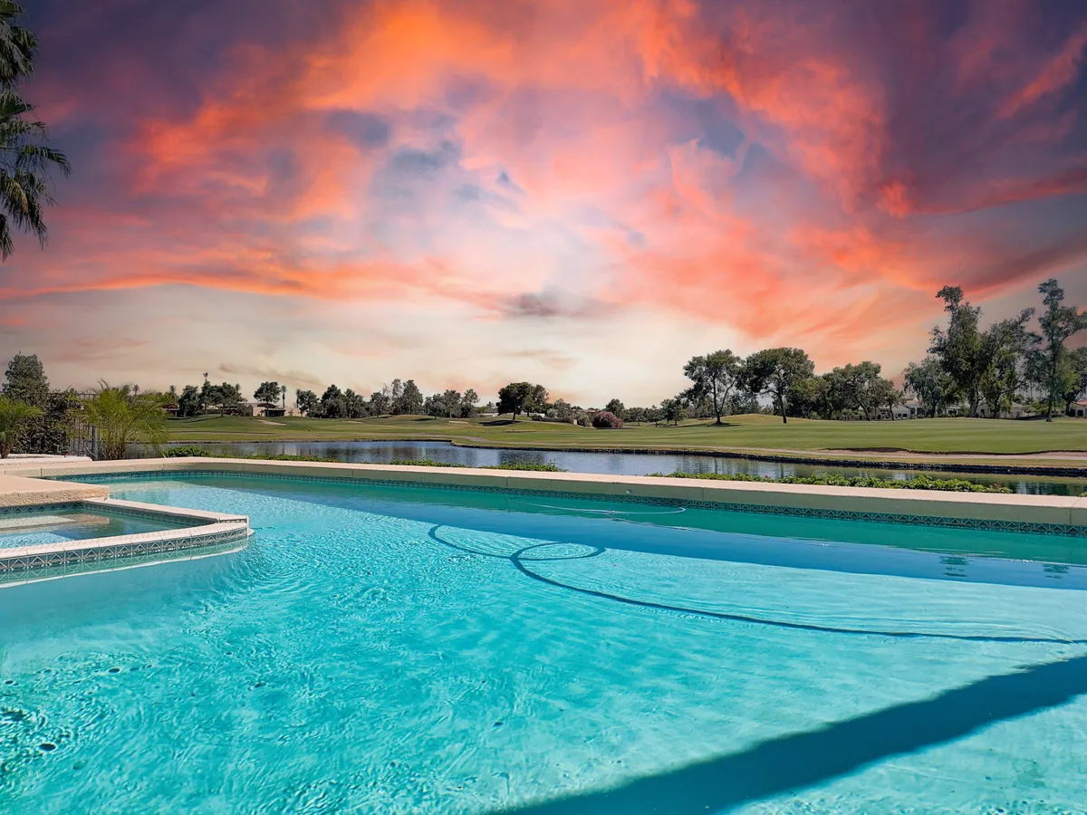 A serene backyard setting with a swimming pool, integrated spa, lush greenery, and a spectacular sunset sky. The image includes views of the adjacent golf course, enhancing the sense of luxury and exclusivity.
