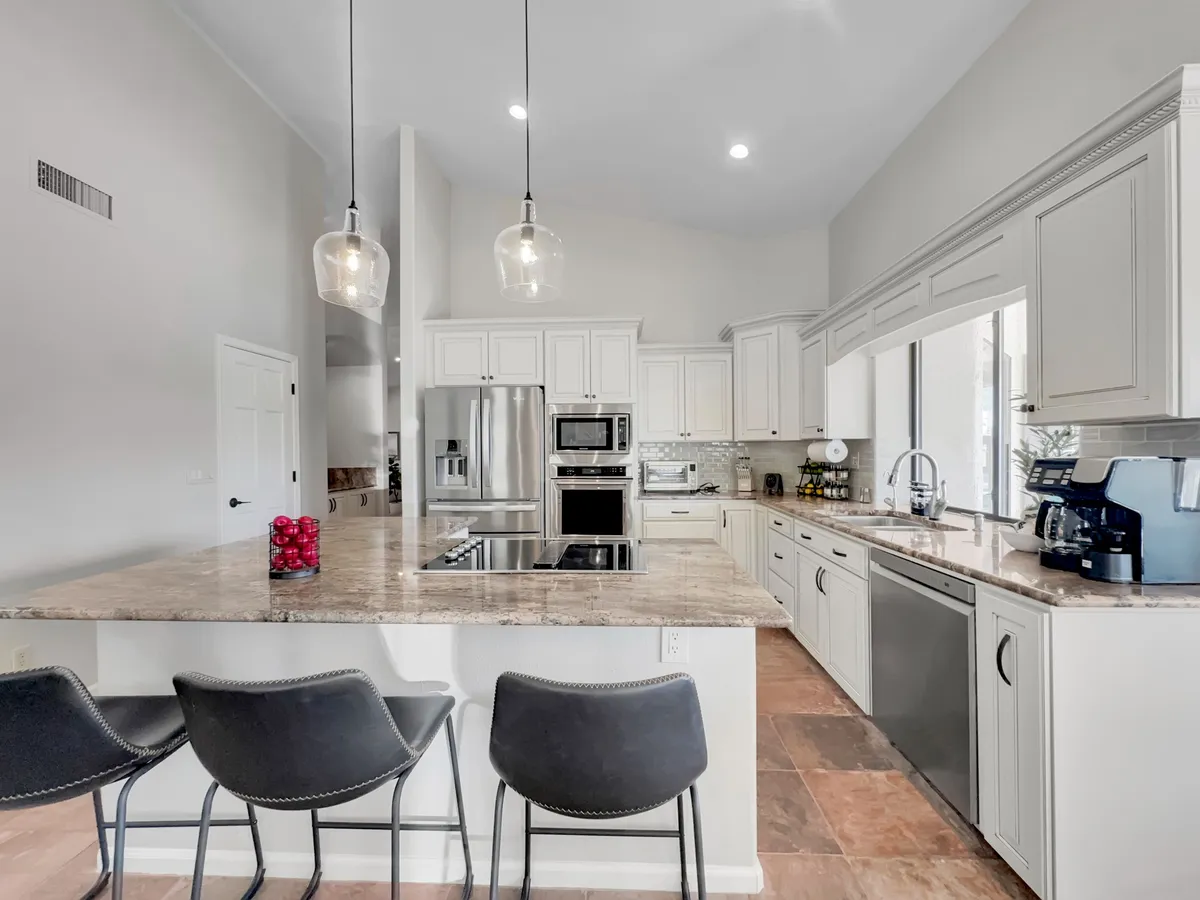 This image shows a spacious, modern kitchen featuring a large granite countertop island, stainless steel appliances, and stylish pendant lighting. The space is bright and welcoming, ideal for preparing meals and hosting gatherings.