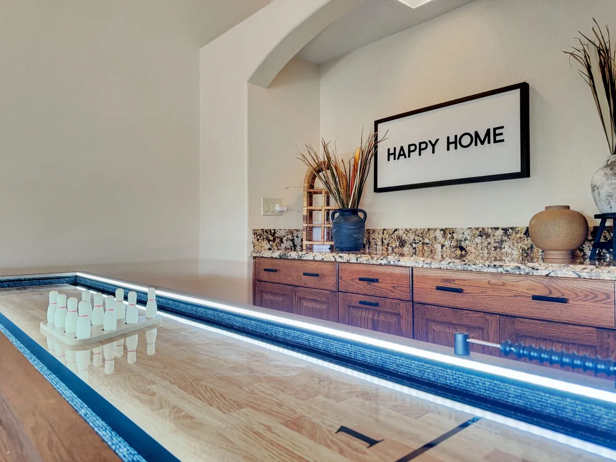 A cheerful game room scene, complete with a granite countertop and a playful bowling pin set on display. The décor includes a 'HAPPY HOME' sign and vibrant plants, creating an inviting atmosphere for fun, laughter, and group activities.