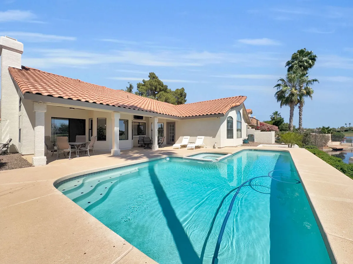 This exterior image showcases a luxurious swimming pool, comfortable outdoor seating, tall palm trees, and the house's contemporary architecture. The serene water, inviting patio area, and lush landscaping create an atmosphere of resort-style relaxation.