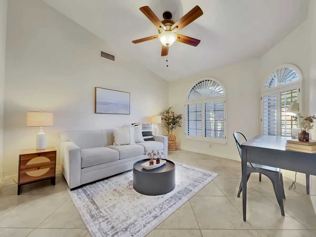 A comfortable seating area with a sofa, coffee table, and a dedicated desk and lamp by the window. The room is bathed in soft, natural light and decorated in neutral, calming tones, offering a relaxing environment for work or leisure.
