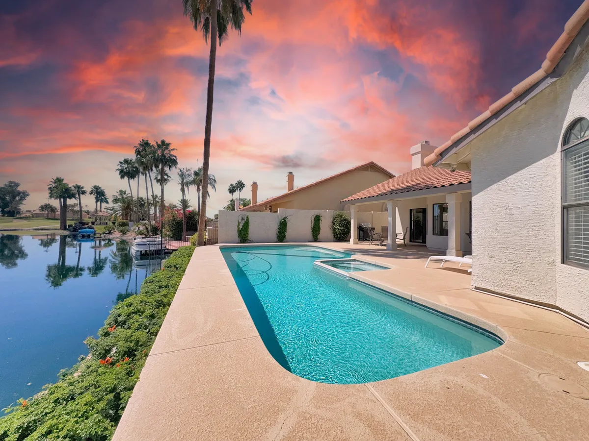 A luxurious swimming pool surrounded by palm trees, reflecting the vibrant colors of a sunset sky. Loungers are arranged beside the pool, and the tranquil water mirrors the evening light, setting a relaxing mood for poolside gathering.