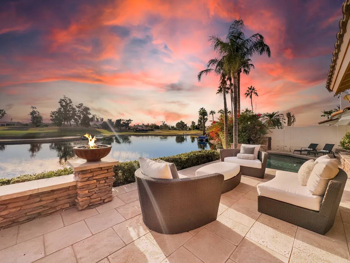 A cozy outdoor seating area with a fire pit overlooking water and palm trees, set under a breathtaking sunset sky. The arrangement invites evening socializing, relaxation, and stargazing.